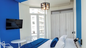 Et moderne hotelværelse med en stor seng, et tv ophængt på væggen, et lille hvidt bord og en stol.