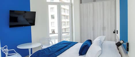 A modern hotel room with a large bed, a TV mounted on the wall, a small white table, and a chair.