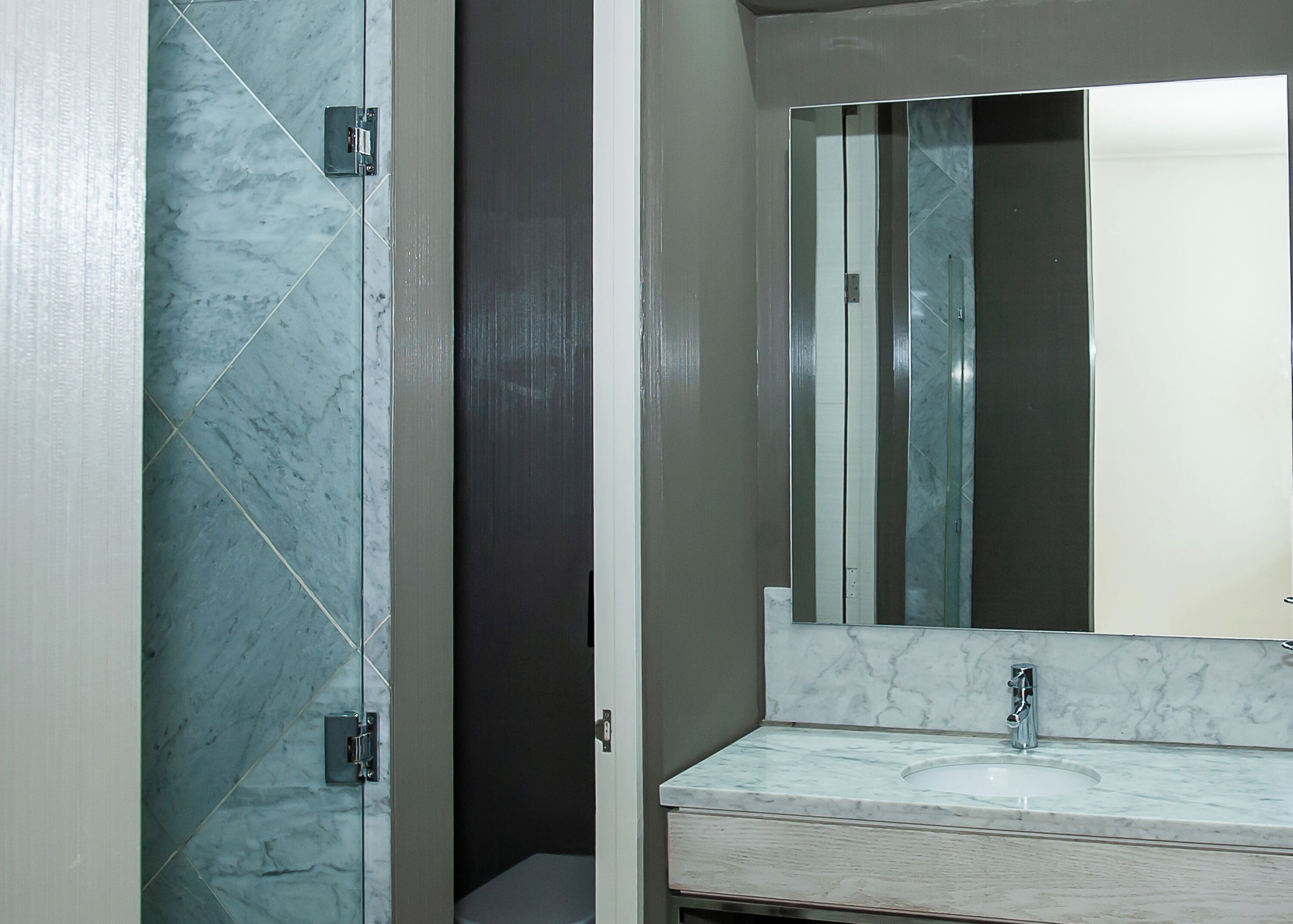 Un baño con lavamanos de mármol, un espejo grande y una puerta de ducha.