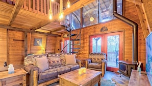 A cozy cabin interior with a wooden interior, a spiral staircase, a fireplace, and a large window.