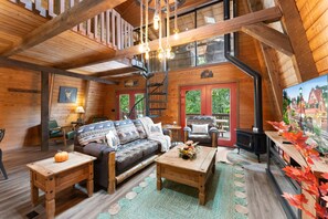 A cozy cabin interior with a wooden ceiling, a sofa with patterned cushions, a coffee table, and a fireplace.