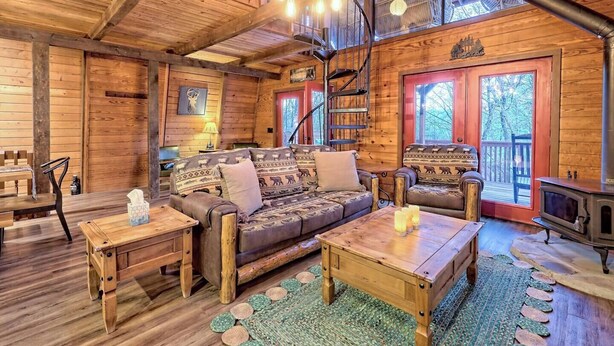 A cozy cabin interior with a wooden interior, a fireplace, a sofa, and a dining table.