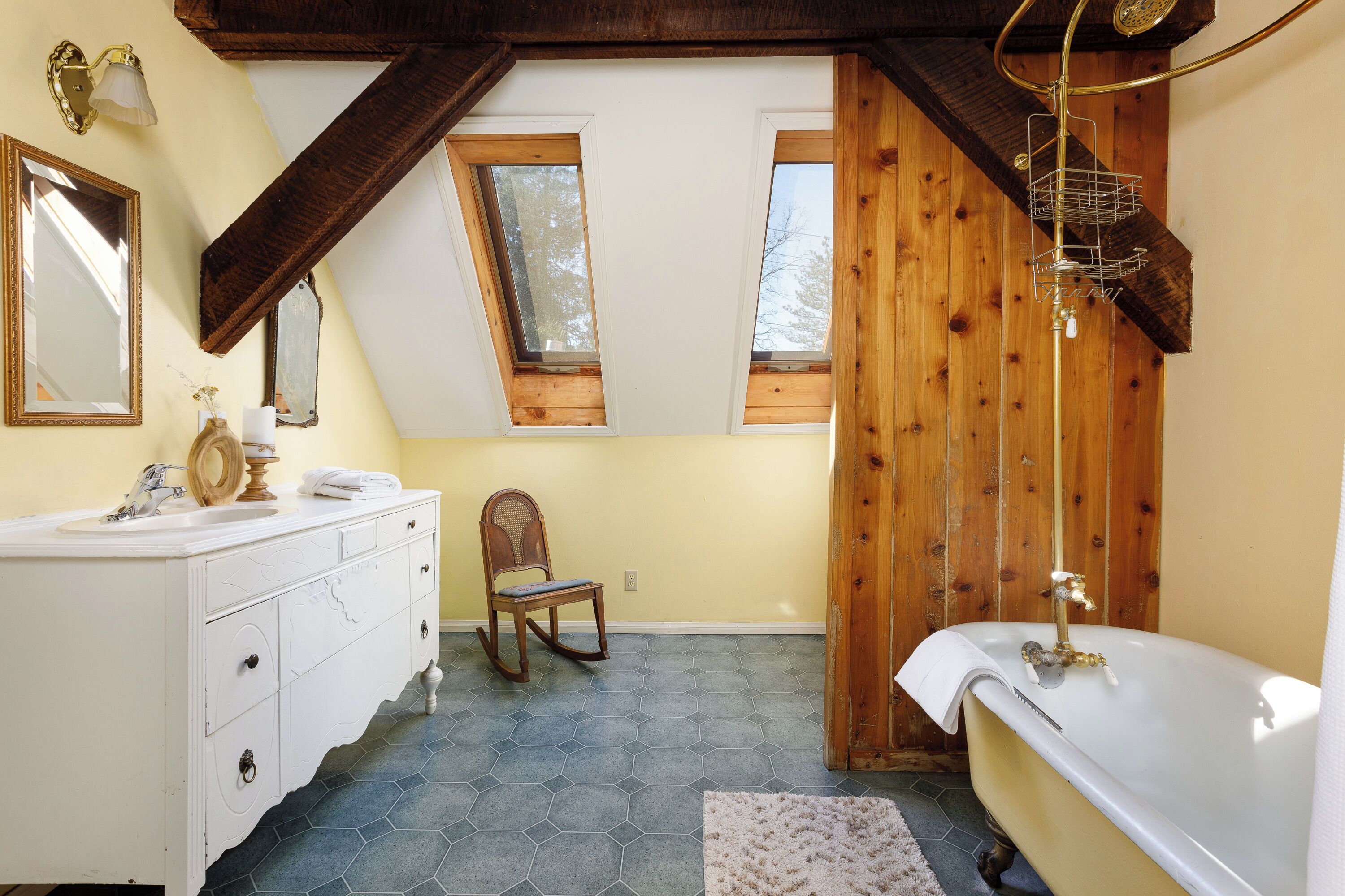 Ein Badezimmer mit weißem Waschtisch, einem Holzschaukelstuhl, einer Badewanne und einem Dachfenster.