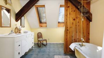 A bathroom with a white vanity, a wooden rocking chair, a bathtub, and a skylight.