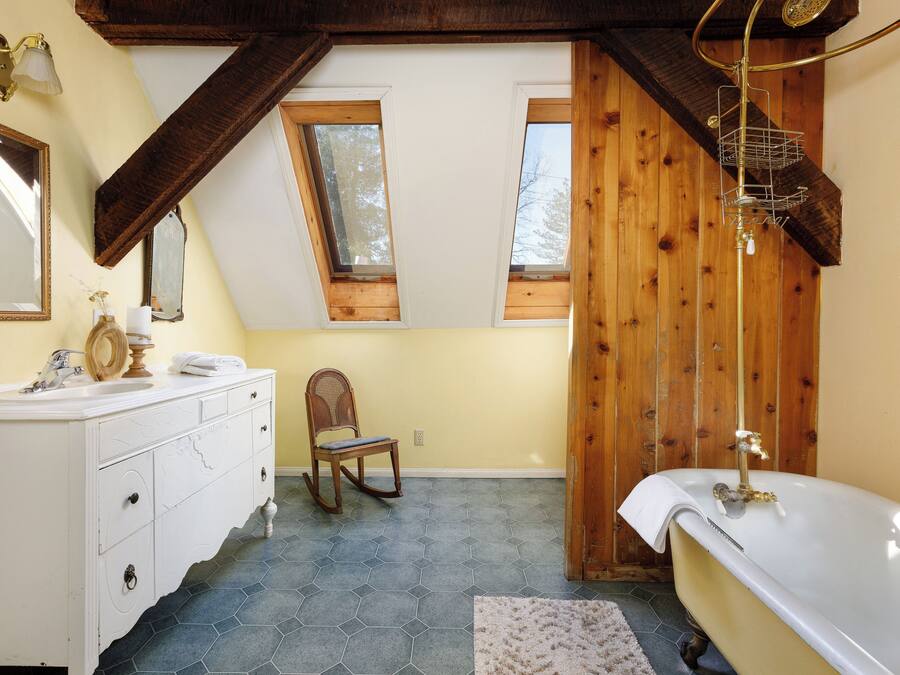 A bathroom with a white vanity, a wooden rocking chair, a bathtub, and a skylight.