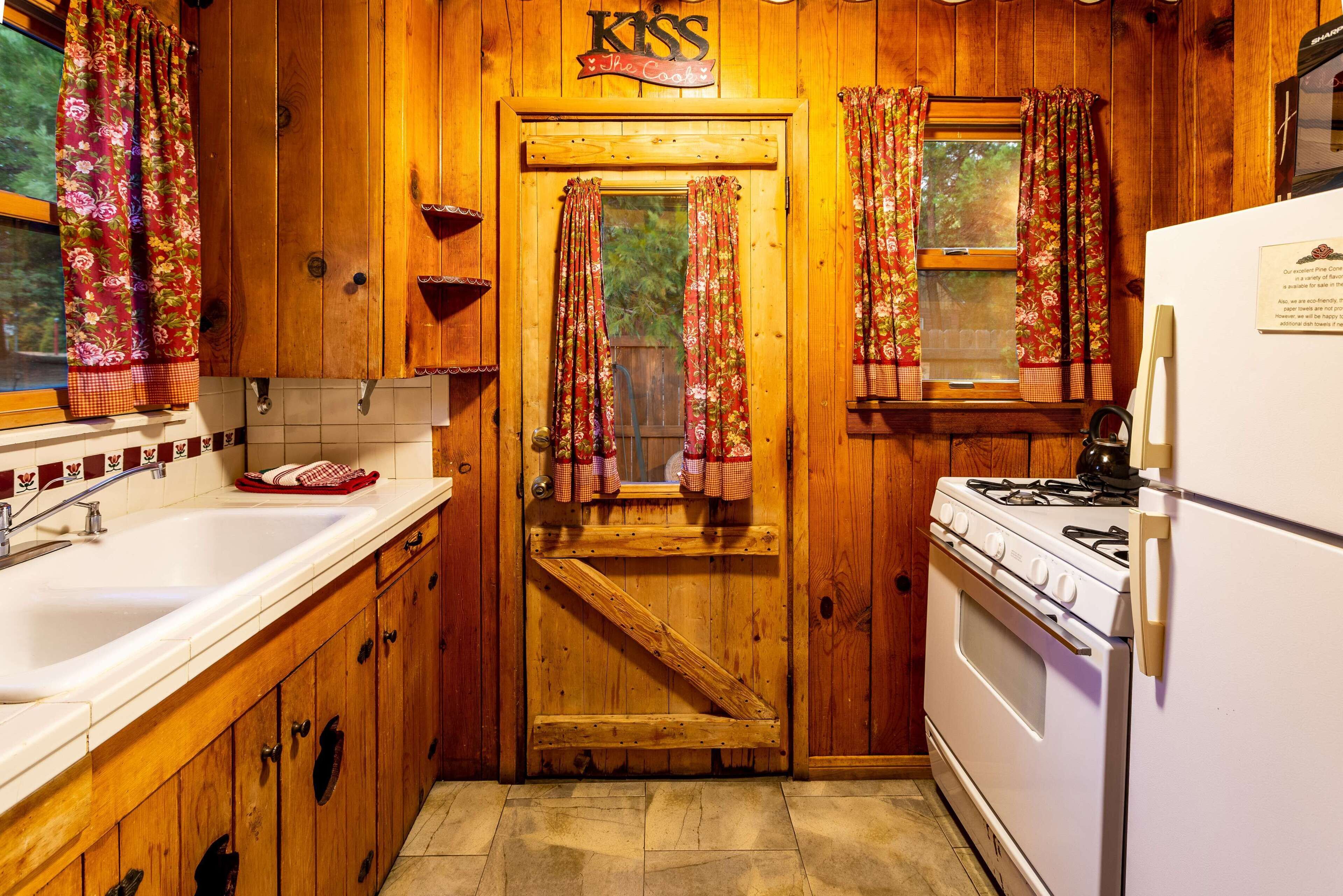 A wooden kitchen with a sink, stove, and a door with curtains.