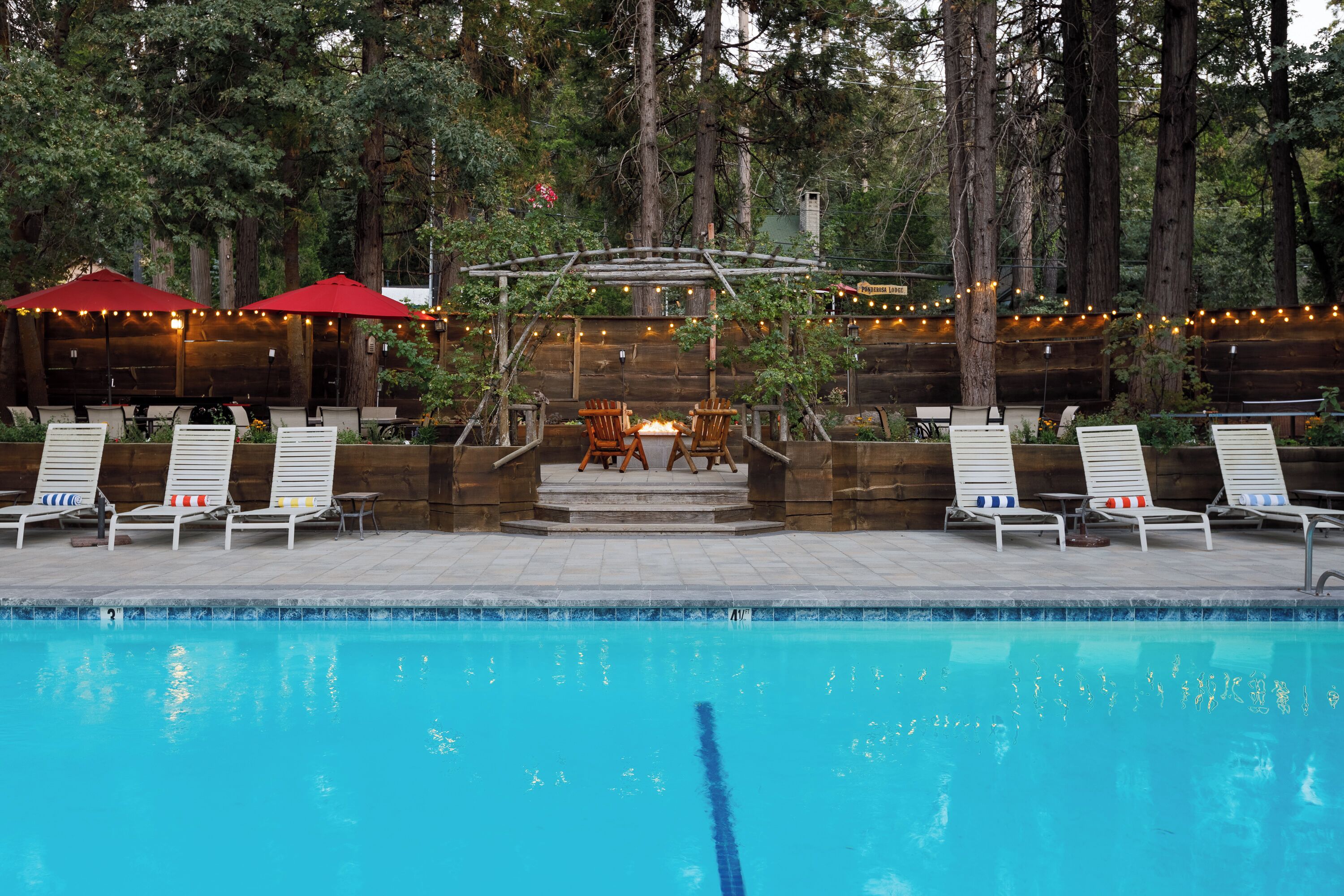 A pool area with lounge chairs and a pergola with string lights.