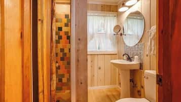 A wooden interior with a wooden floor, a white toilet, a sink with a mirror, and a window with curtains.