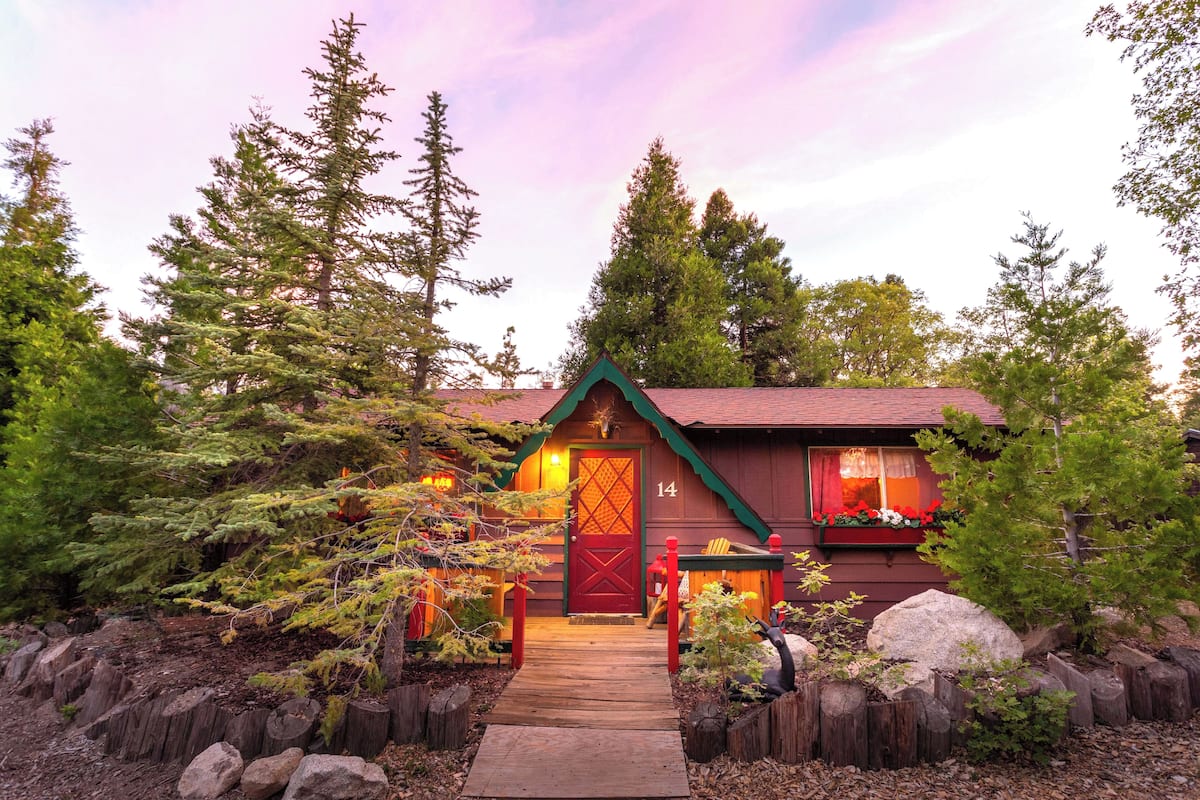 Un chalet rustique avec une porte rouge, une terrasse en bois et un chemin de pierre menant à l’entrée.