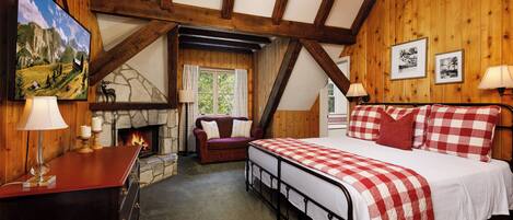 Una habitación acogedora con chimenea, una cama con ropa de cama a cuadros, un escritorio con lámpara y paredes de madera.