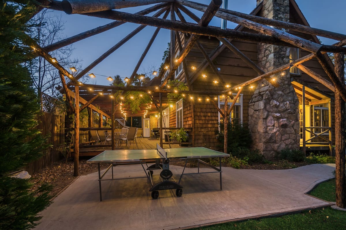 Un espace extérieur rustique agrémenté d’une table de ping-pong, de guirlandes lumineuses et d’une structure de pergola en bois.