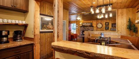 A rustic kitchen with wooden cabinets, a coffee maker, and a bench.