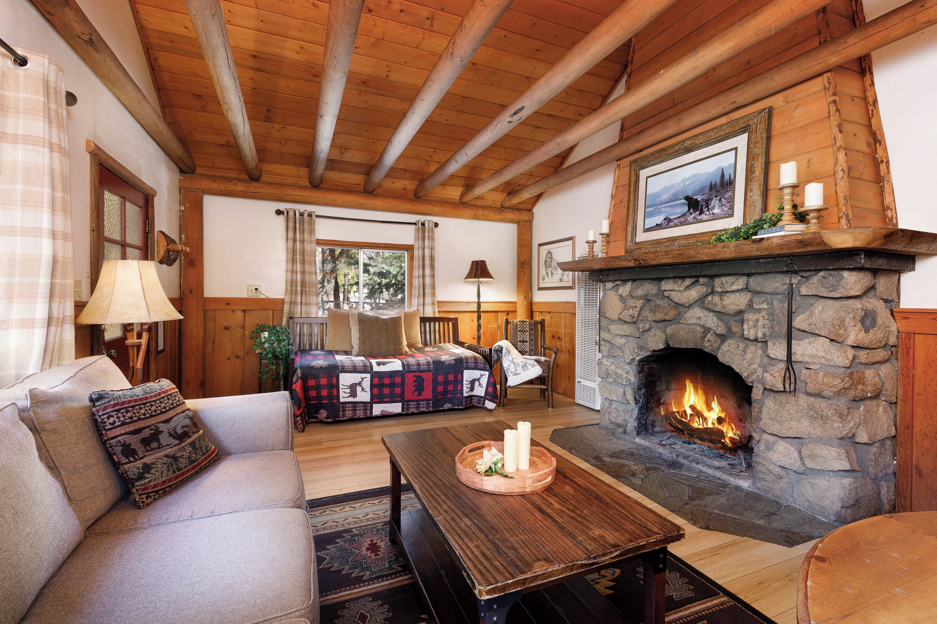 A cozy living room with a stone fireplace, wooden beams, a sofa, and a coffee table.