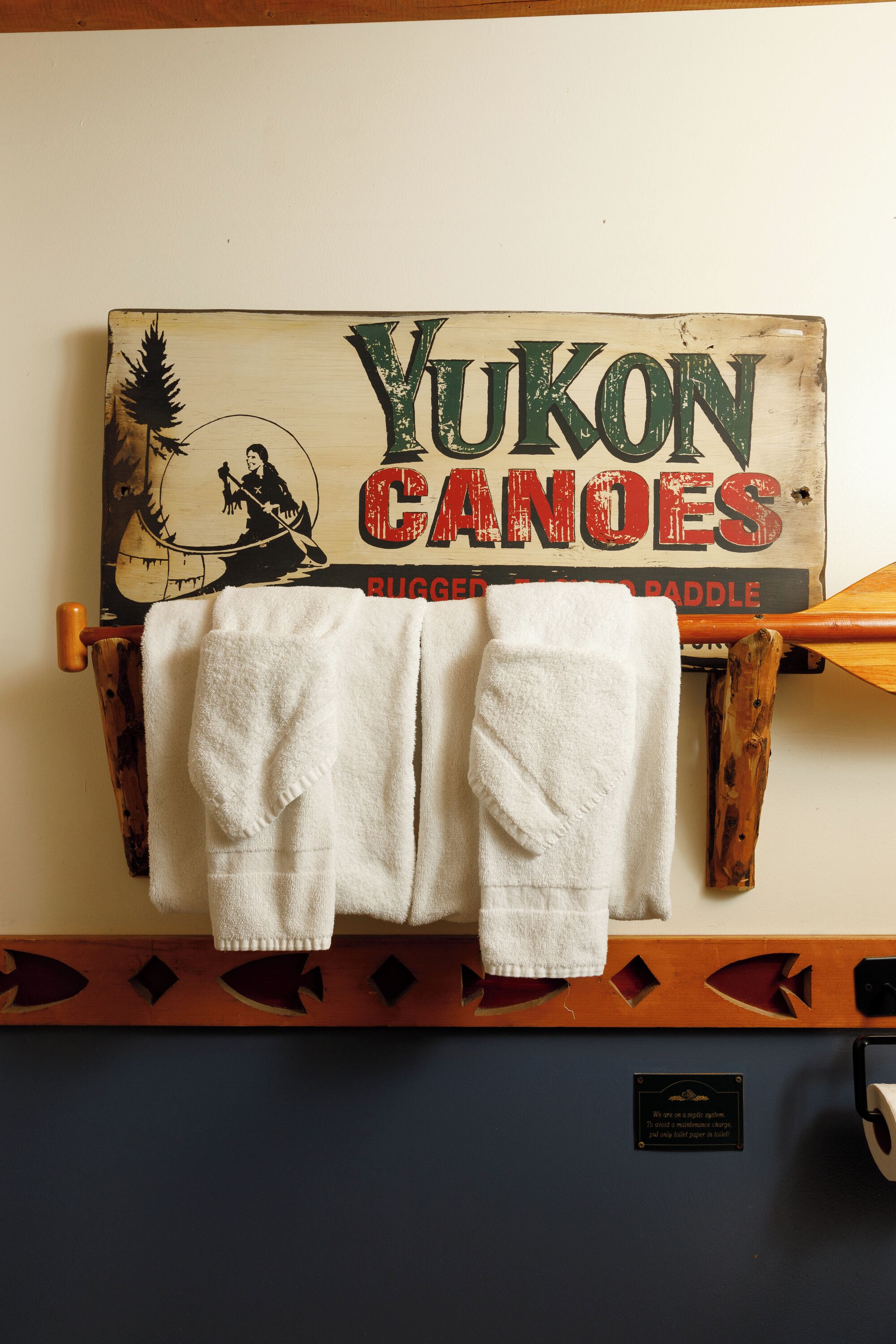 Een bord aan de muur met de tekst 'Yukon Canoes' en een houten peddel die ertegen leunt.