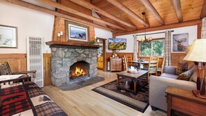 Una sala de estar acogedora con chimenea de piedra, vigas de madera, un sofá confortable, una mesa de comedor y un televisor.
