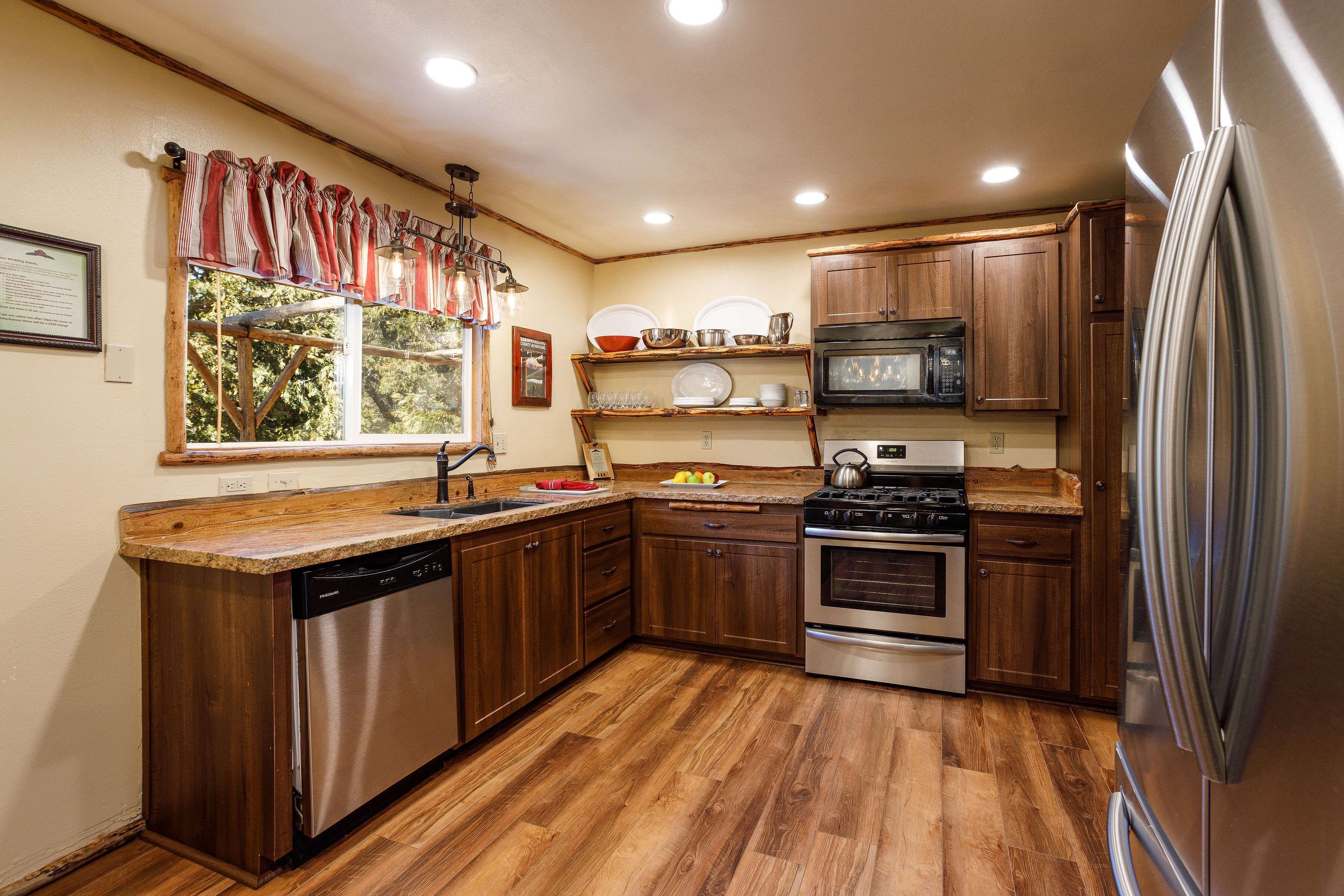 Cocina con armarios de madera, electrodomésticos de acero inoxidable y una ventana con cortinas.