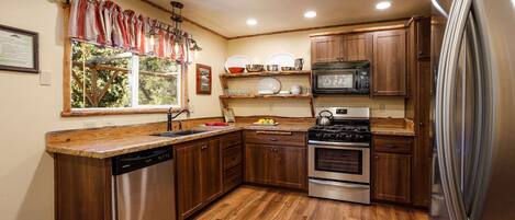 Cocina con armarios de madera, electrodomésticos de acero inoxidable y una ventana con cortinas.