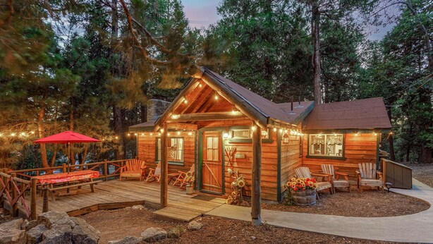 Una cabaña de troncos con terraza, asientos exteriores y luces colgantes.
