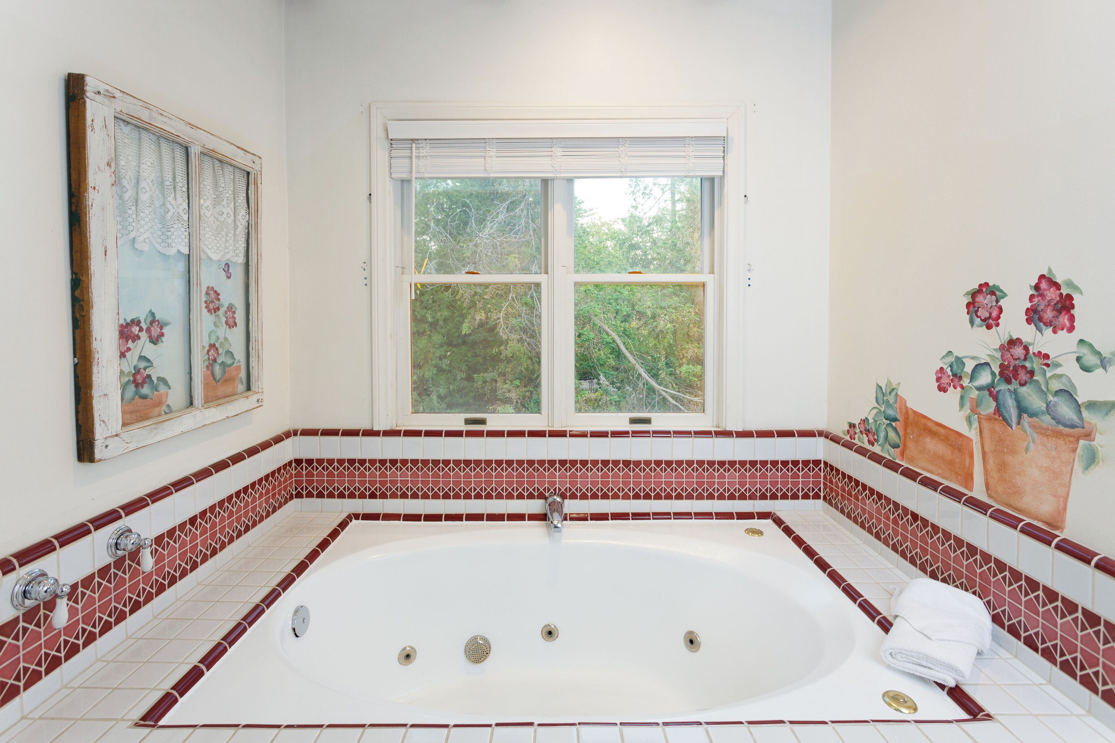 A bathroom with a large bathtub, a window with blinds, and a decorative wall with floral patterns.