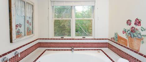 A bathroom with a large bathtub, a window with blinds, and a decorative wall with floral patterns.