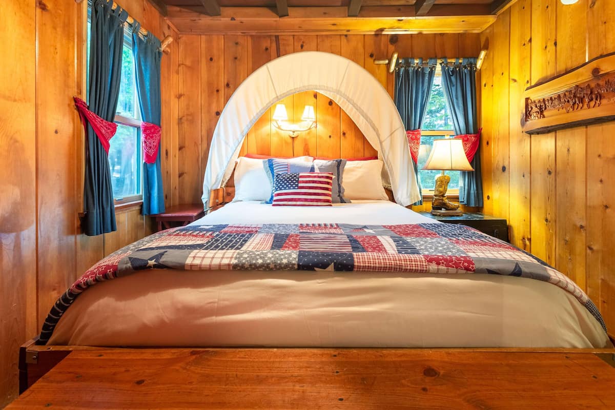 Une chambre à coucher dans une cabane en bois, avec un lit à baldaquin, une courtepointe ornée d’un motif patriotique et une décoration rustique.