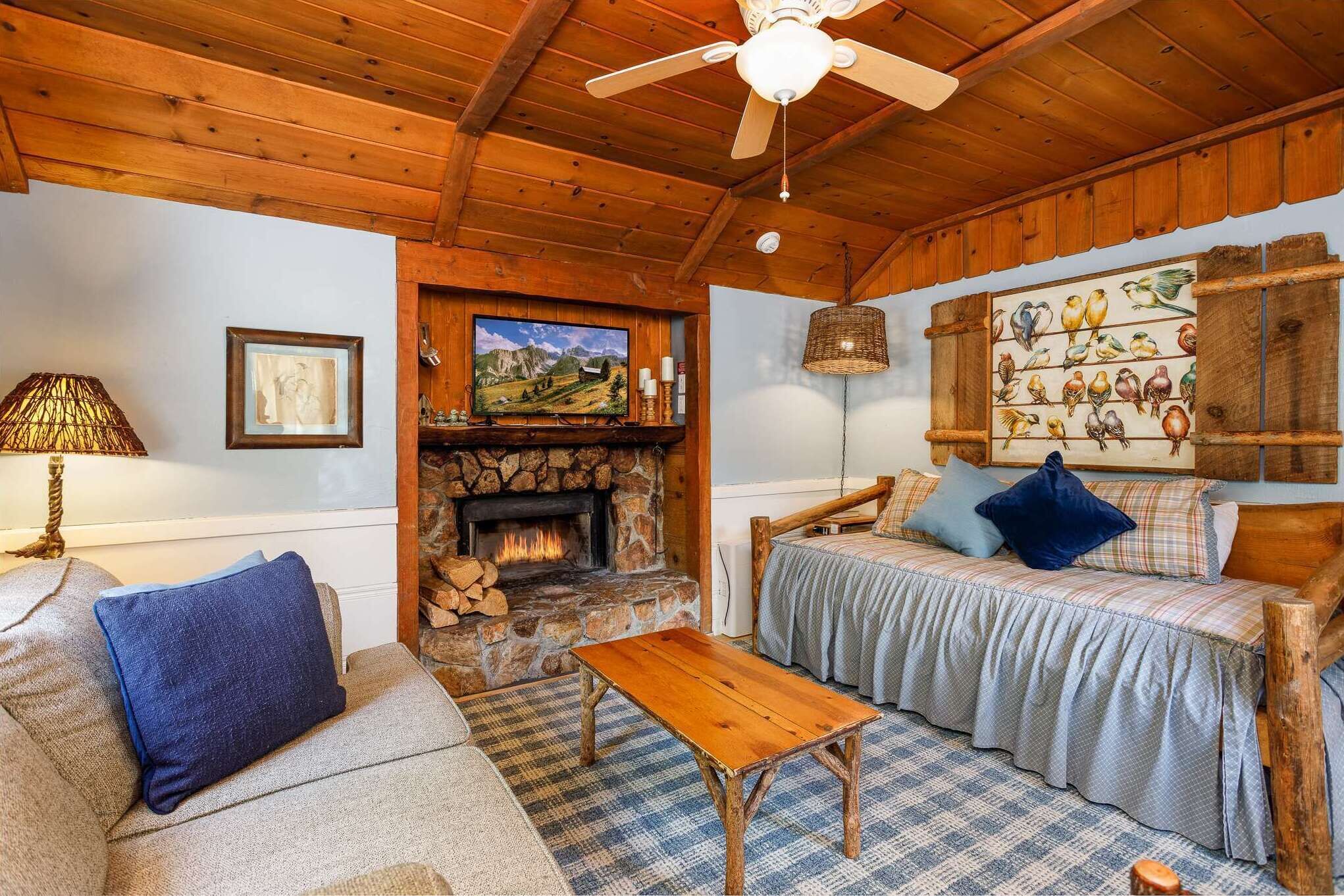 A cozy room with a stone fireplace, wooden ceiling, and a bed with blue bedding.