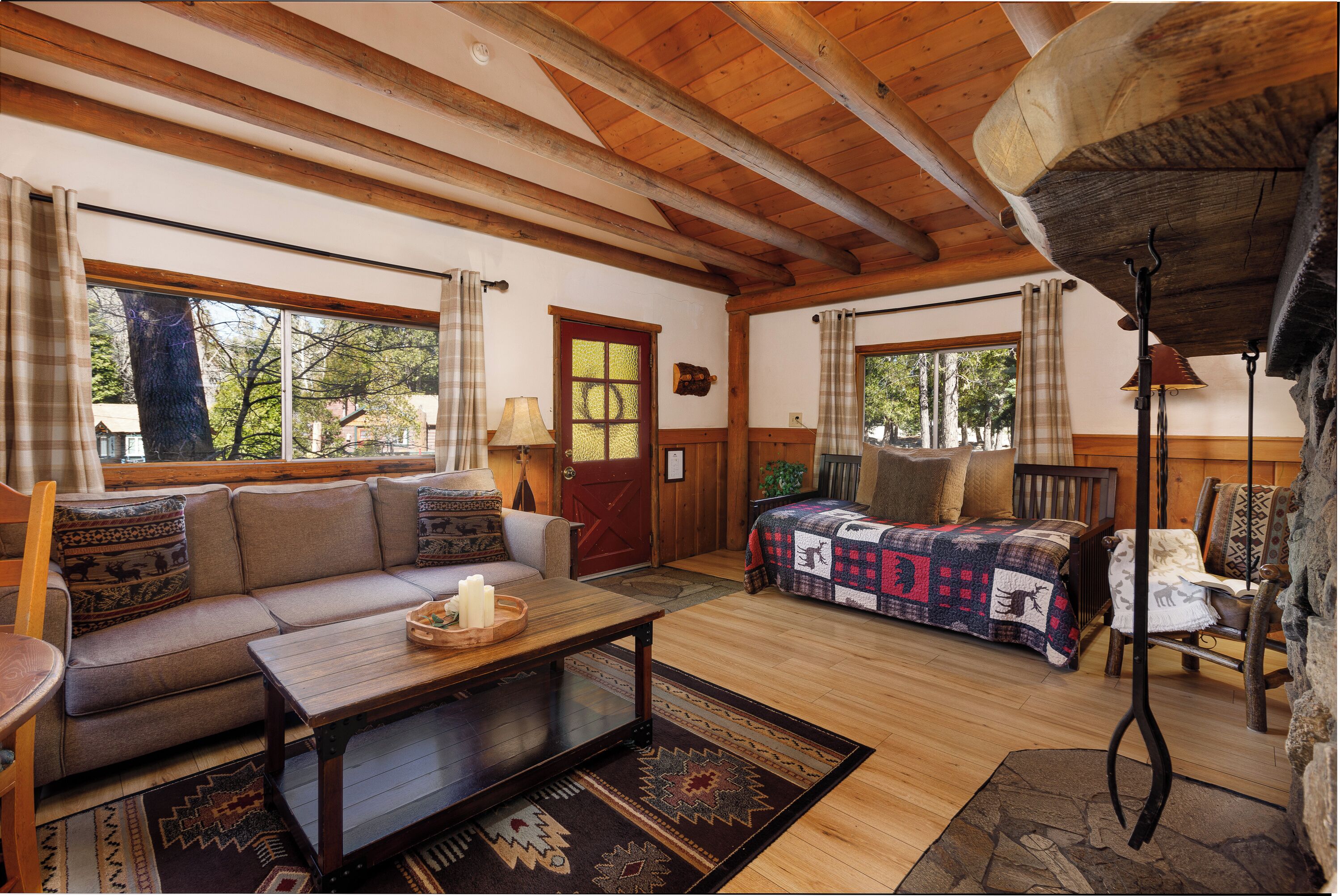 Interior acogedor de una cabaña con techo de madera, un sofá, una cama con colcha, una mesita de centro y una chimenea.
