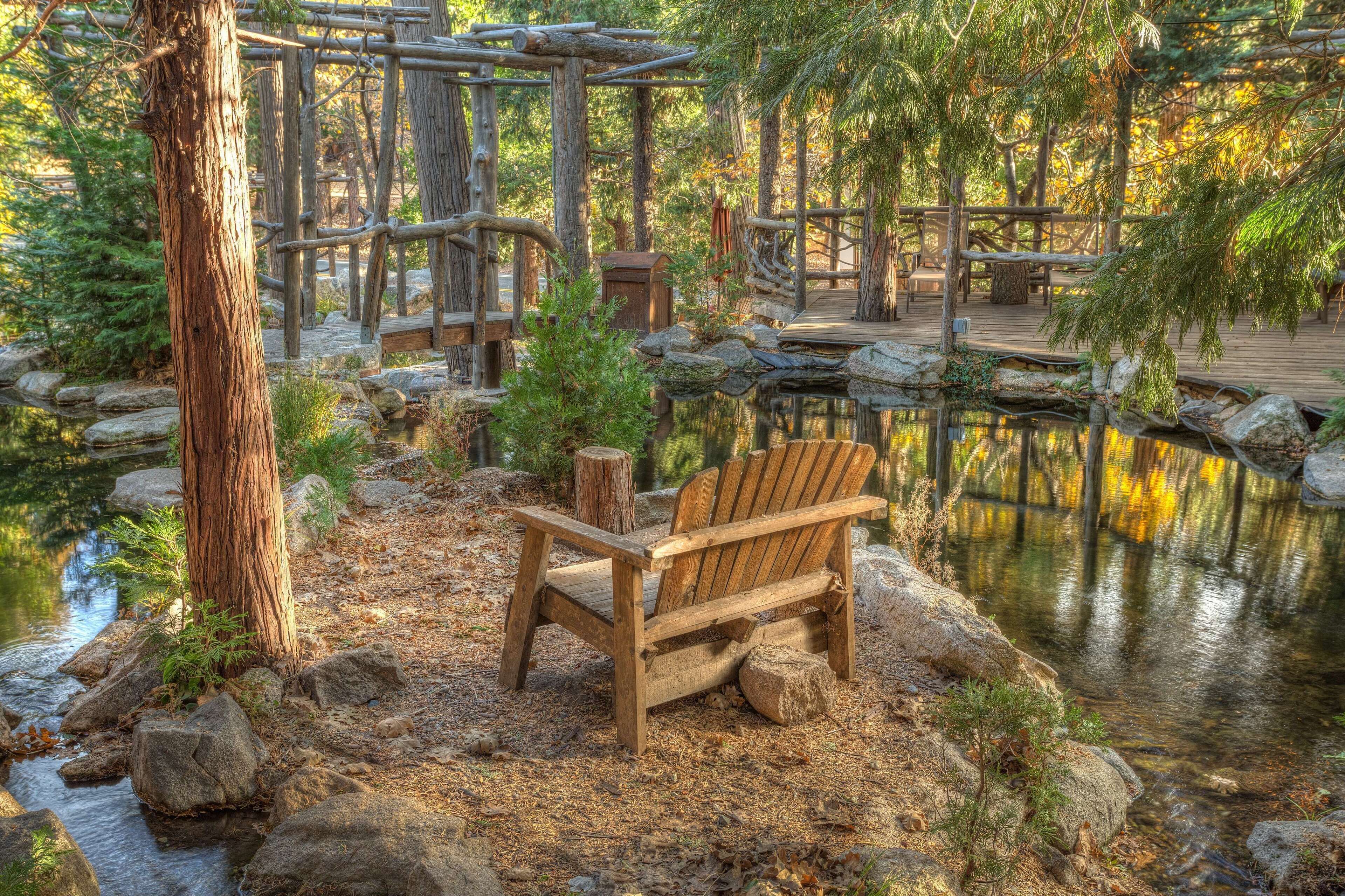 A wooden bench near a pond with a wooden deck and rustic wooden structures in the background.