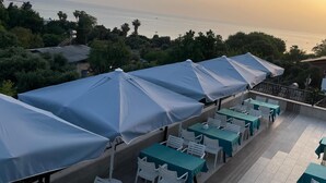 Terraza con mesas y sillas, cubierta por sombrillas azules, con vista a un cuerpo de agua.