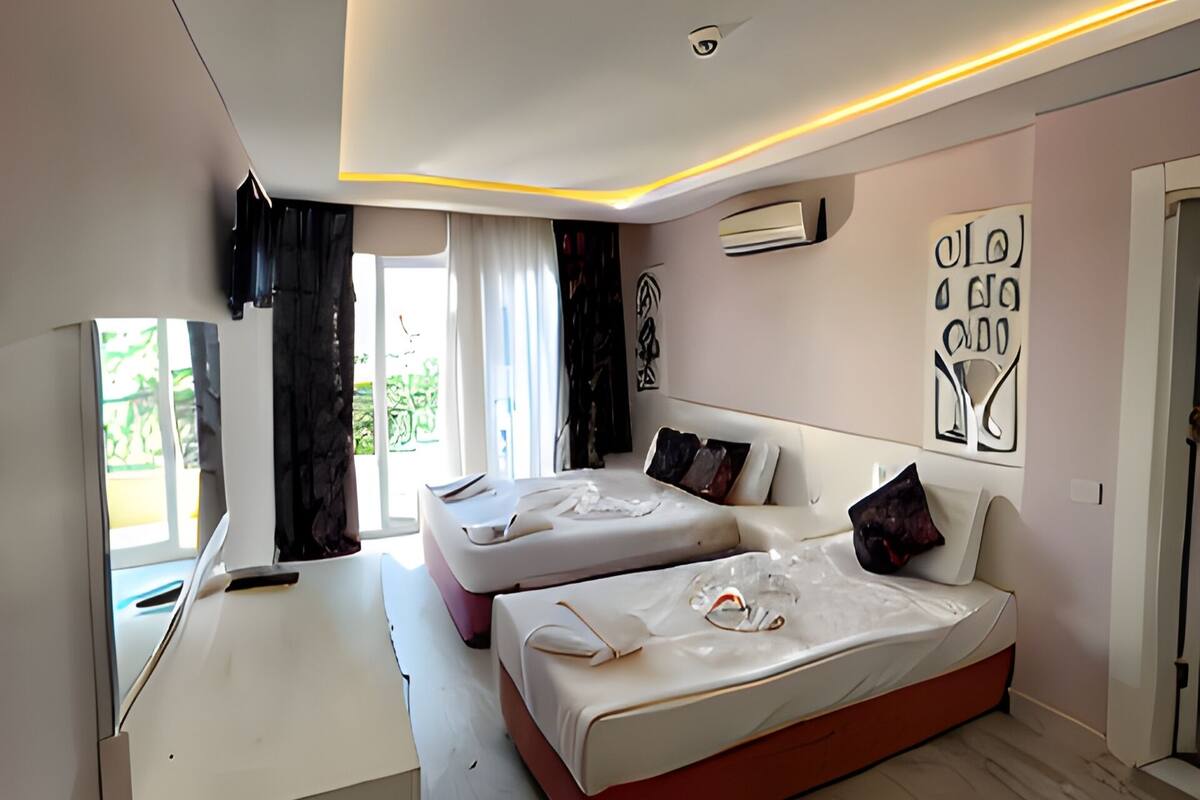 A modern bedroom with two beds, a desk, and a large window.
