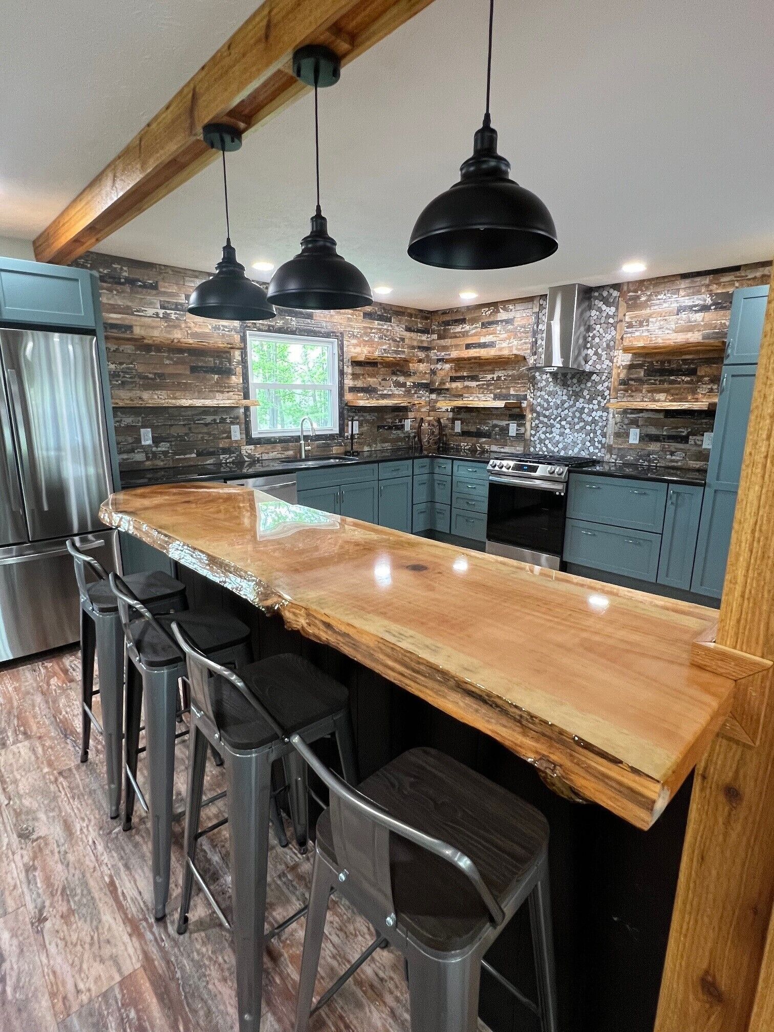 A modern kitchen with a wooden island, bar stools, and a stainless steel refrigerator.
