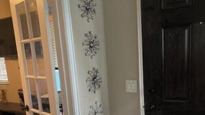 A hallway with a dark wooden door, a glass door leading to another room, and decorative wall art. - Charming Crowley Rental (Crowley)