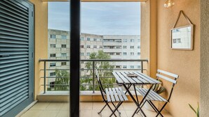 Een balkon met een tafel en stoelen, uitzicht op een gebouw en een hanglamp.