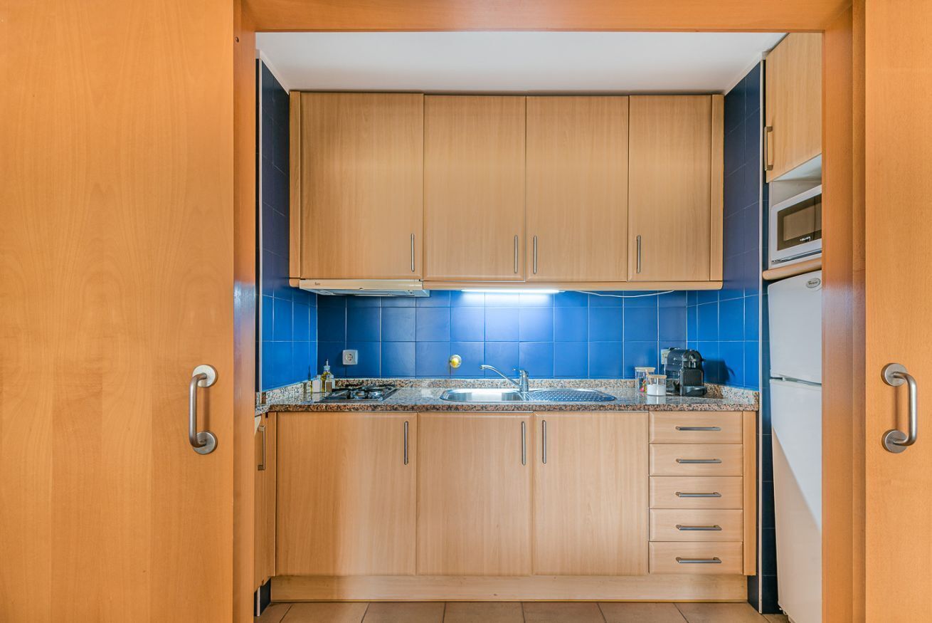 Eine kleine Küche mit Holdekor-Schränken, einer blauen Fliesenrückwand, einer Edelstahl-Spüle und einer Mikrowelle.