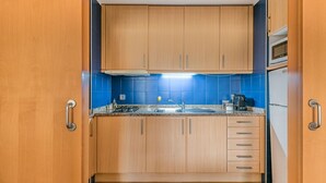 Een kleine keuken met houten kastjes, een blauwe betegelde achterwand, een roestvrijstalen spoelbak en een magnetron.