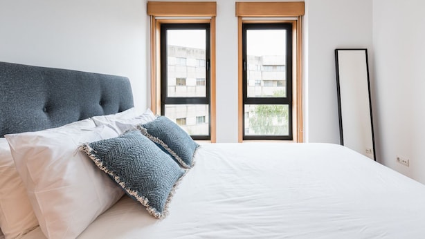 Een slaapkamer met een groot bed, twee ramen en een hoge, zwarte spiegel.