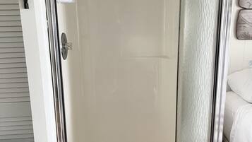 A shower enclosure with a glass door, a showerhead, and a ventilation vent.