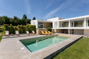 A modern house with a swimming pool, outdoor seating, and a well-maintained garden.