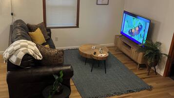 A living room with a leather sofa, a coffee table, a TV, and a patterned rug.