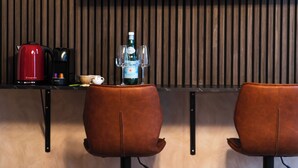 Une cuisine moderne avec un mur recouvert de panneaux en bois, une bouilloire rouge, une machine à café, une bouteille d’eau et deux fauteuils en cuir marron.