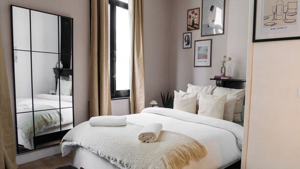 Une chambre bien rangée, avec un grand lit, un miroir et une fenêtre avec des rideaux.