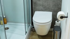 A bathroom with a toilet, a glass shower enclosure, a trash can, and a roll of toilet paper. - Creative Corner: Stylish Apt. in Ghent's Heart (Gent)