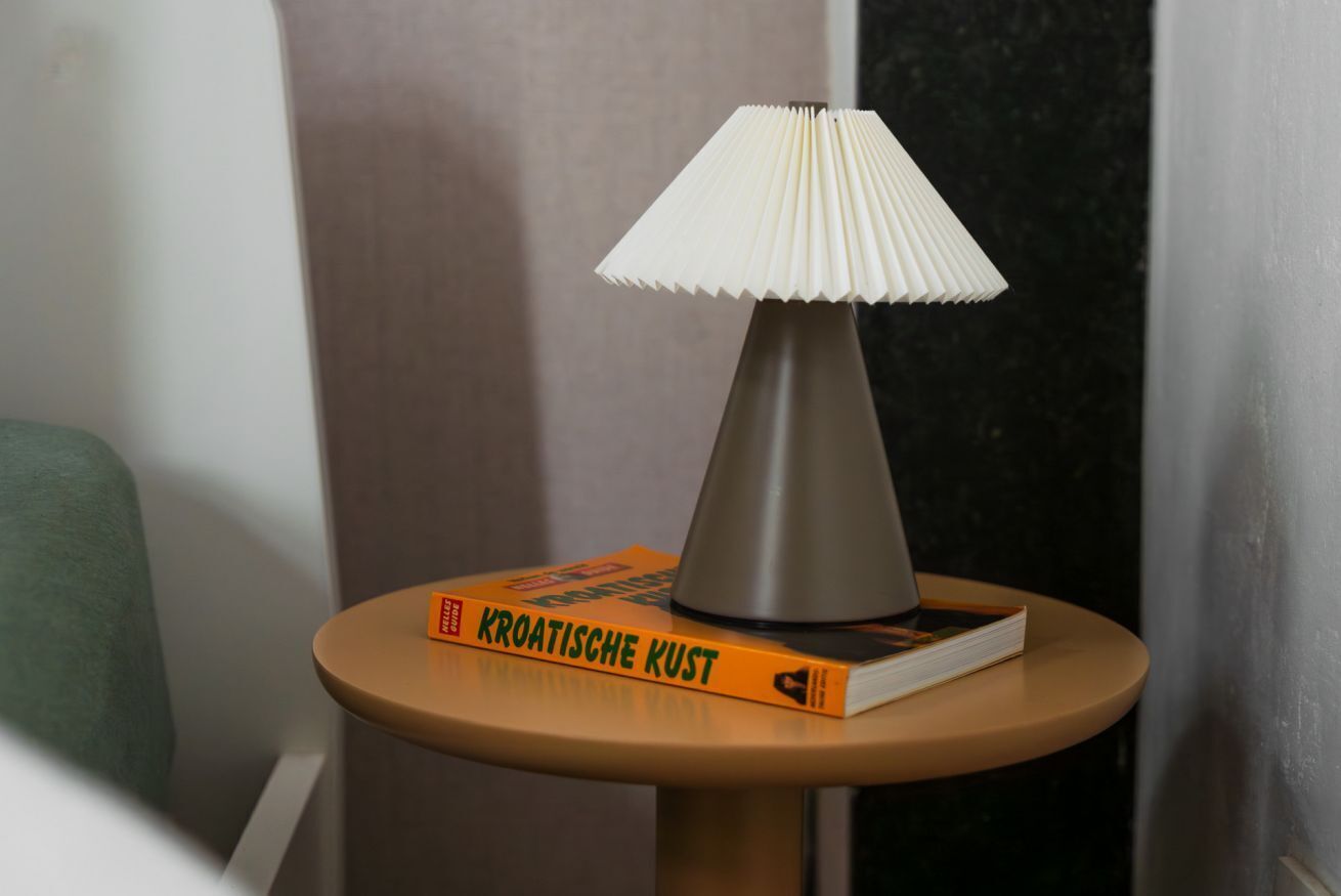 A table with a lamp and a book titled 'KROATISCHE KUST' on it.