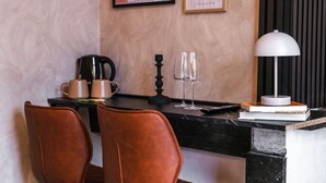 A modern room with a black marble counter, two brown leather chairs, a coffee maker, wine glasses, a lamp, and framed pictures on the wall.