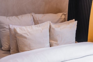 Ein Bett mit weißer Bettwäsche und Kissen, ein Kopfteil und eine dunkel gefärbte Wand.