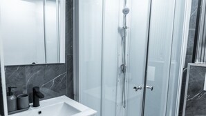 Een moderne badkamer met een douchecabine van glas, een witte wastafel en een wand betegeld met marmer.