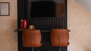 Een moderne kamer met een aan de muur bevestigde televisie, twee leren fauteuils, een rode koffiepot en een lijst met een bericht aan de muur.