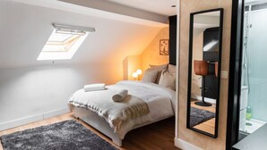 Een slaapkamer met dakraam, een bed met witte deken, een zwarte stoel en een grote spiegel.