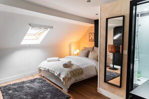 A bedroom with a skylight, a bed with a white blanket, a black chair, and a large mirror.