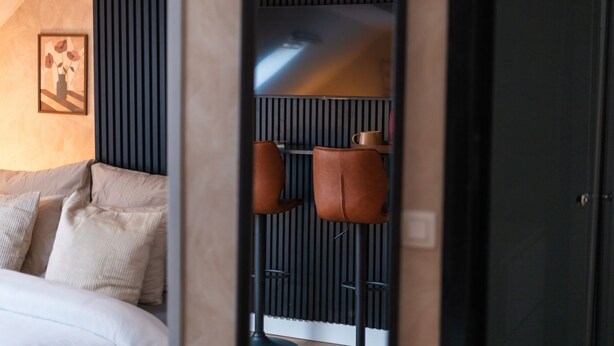 Een moderne hotelkamer met een bed, een ingelijst kunstwerk, een zithoek met stoelen en een donkerbruine garderobe.